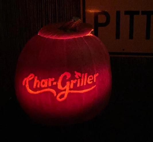 A pumpkin carved with the Char-Griller logo glows in the darkness