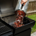 A person pours burning charcoal from a charcoal chimney into the base of the charcoal side of a FlexFuel Grill