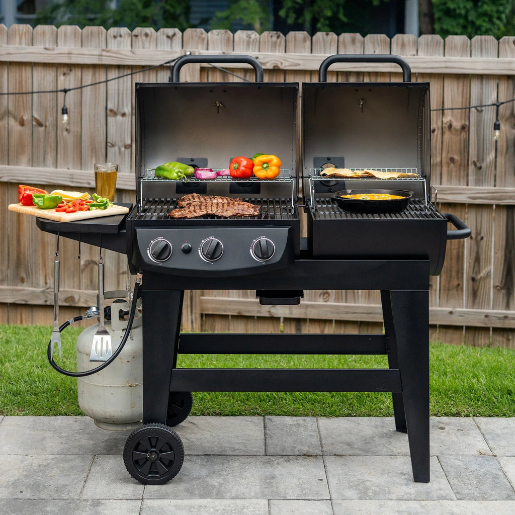 An open Dual-Fuel Pro grill on a paved patio in front of a strip of lawn and a wooden privacy fence. A wooden board holding sliced bell peppers and a stack of tortillas sites next to a full drink glass on the left side shelf. Tongs and a long-handled fork hang from the utility hooks. A propane gas tank is mounted on the left side of the grill cart and is connected to the gas side of the grill.