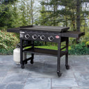 Angled view of the griddle sitting outside on a paved patio. View shows the right side of the griddle, including a handle on the right side shelf.